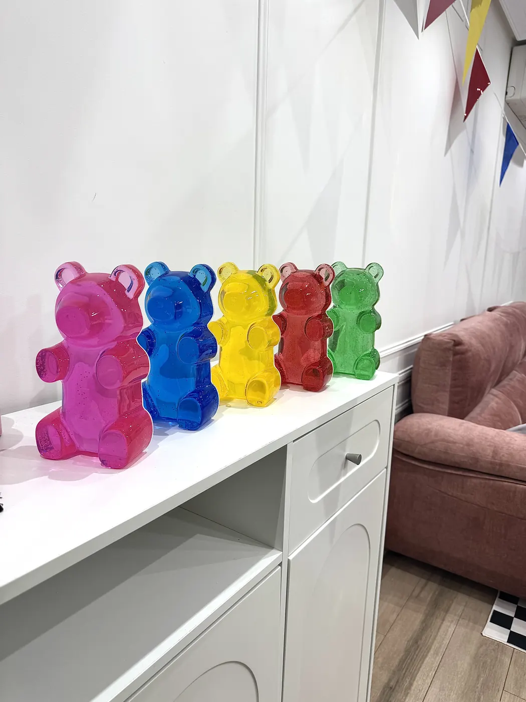 Cinq oursons bonbons géants de couleur alignés sur un meuble blanc