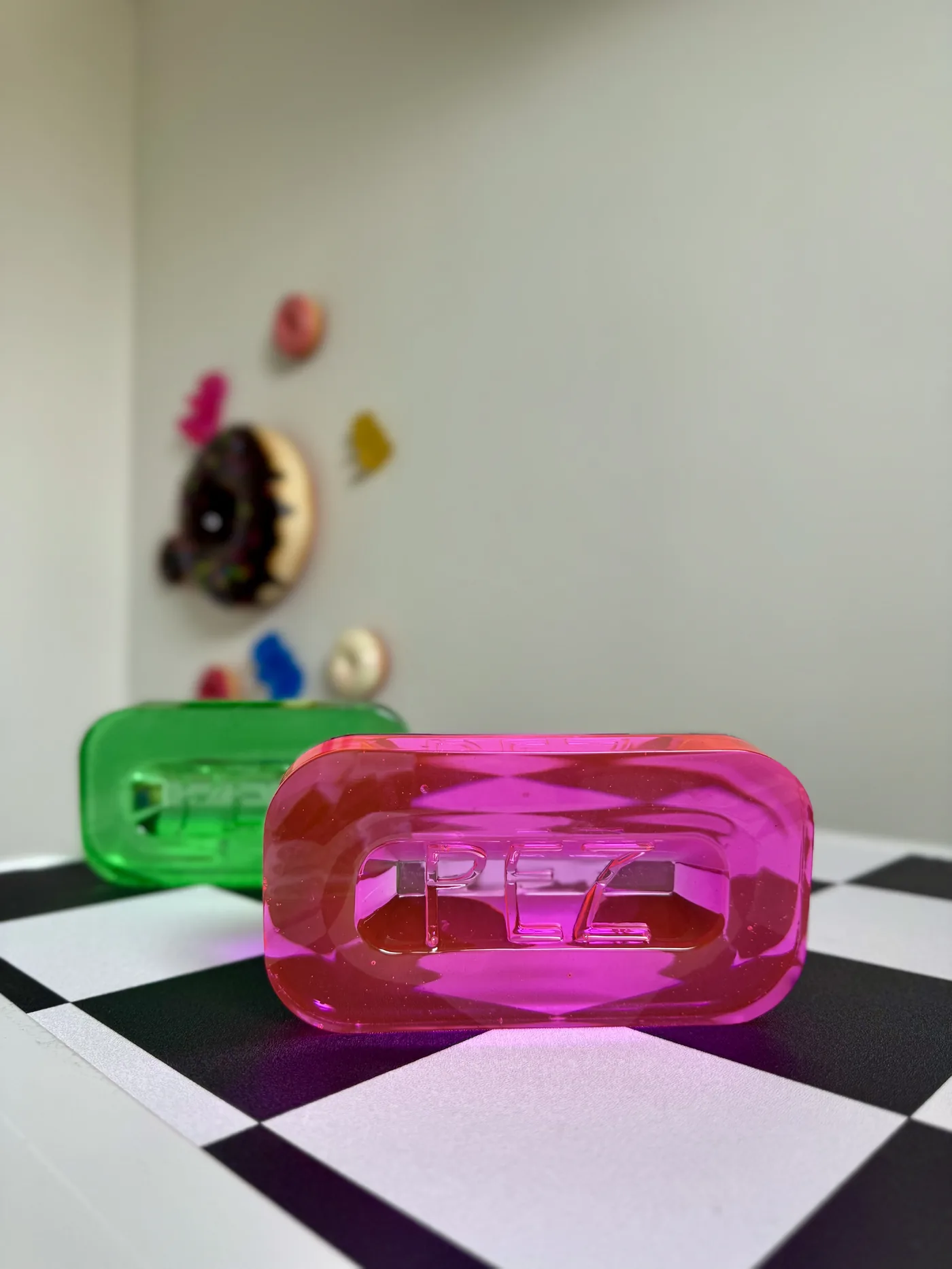 PEZ-Deko-Figuren in Rosa und Grün auf Schachbrettboden, im Hintergrund die Regalwand der Werkstatt