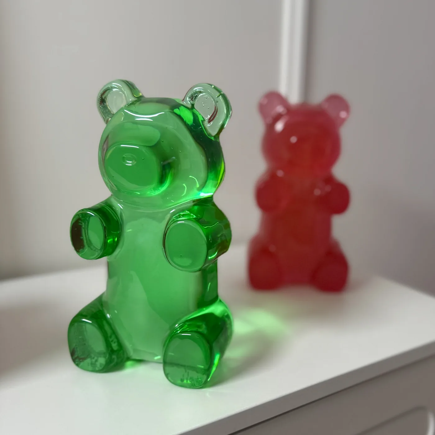 Two resin gummy bears, green and pink, on a white shelf